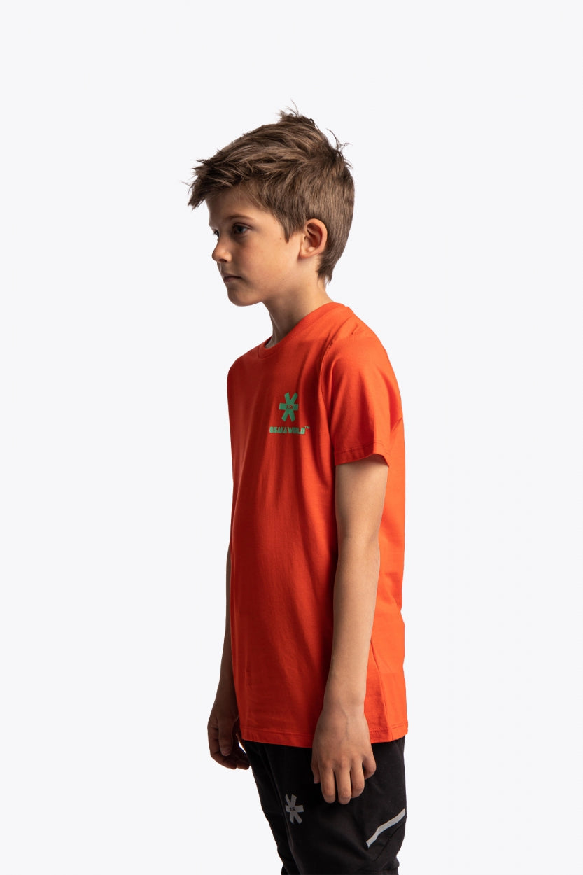 Boy wearing the Osaka kids service games tee short sleeve orange with logo in green. Side view