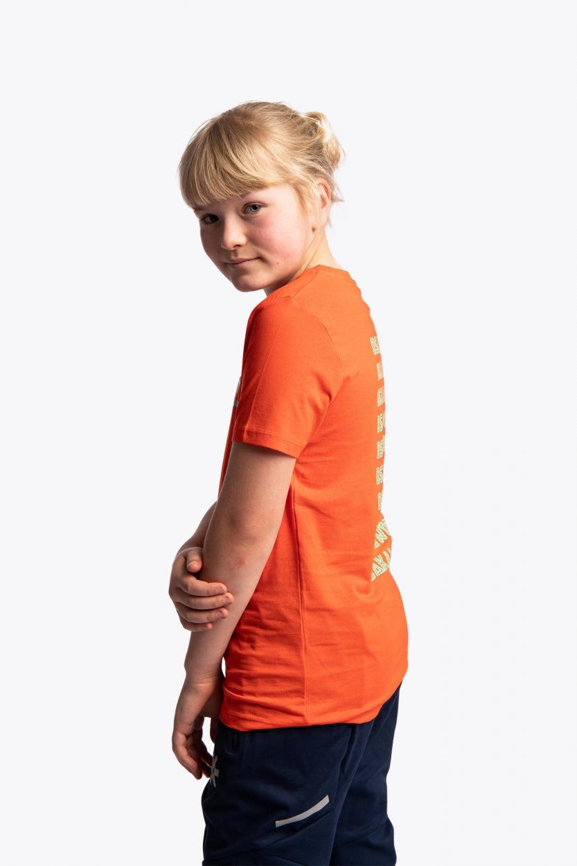 Girl wearing the Osaka kids service games tee short sleeve orange with logo in green. Side view