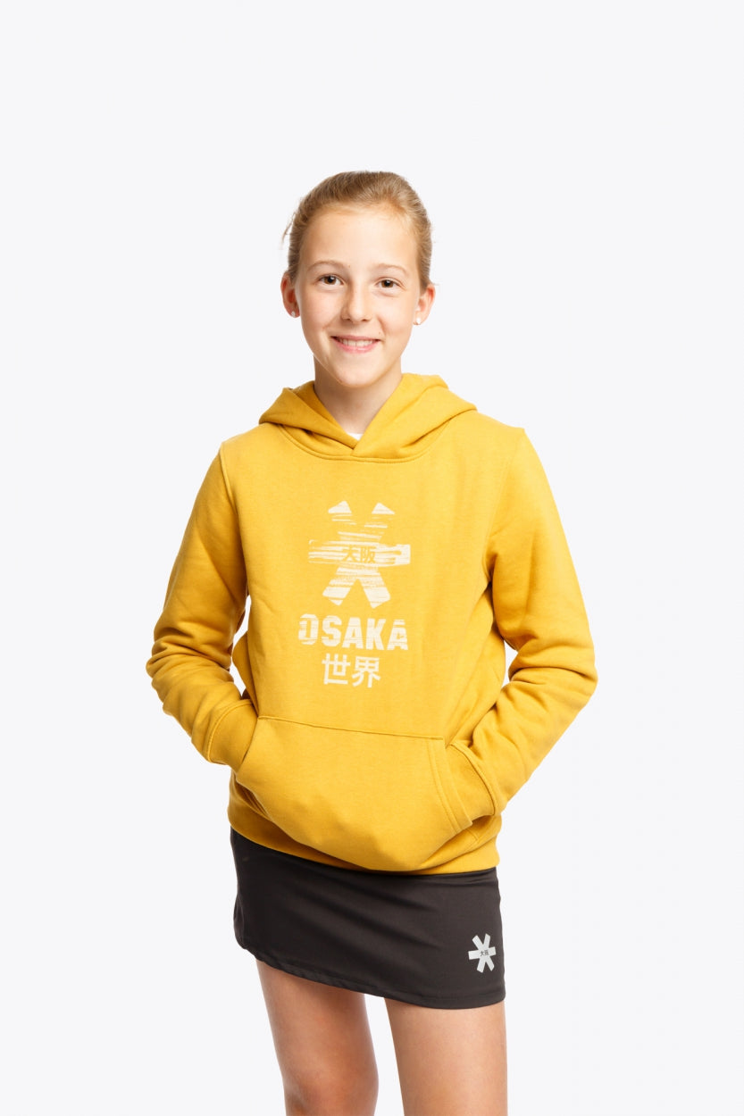 Girl wearing the Osaka kids hoodie in ochre and marker logo in white. Front view