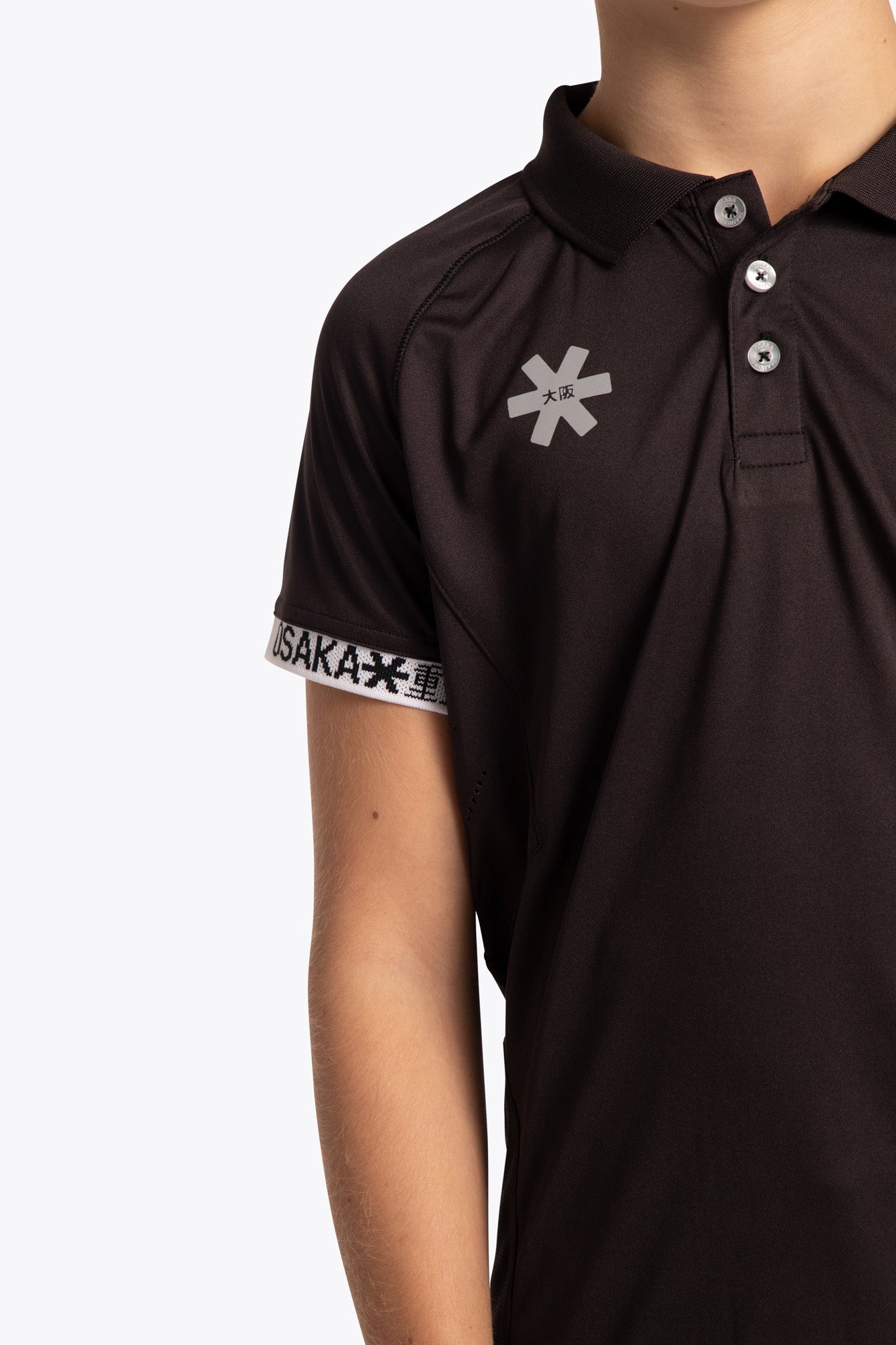 Boy wearing the Osaka Kids Polo Jersey in Black. Front detail logo view