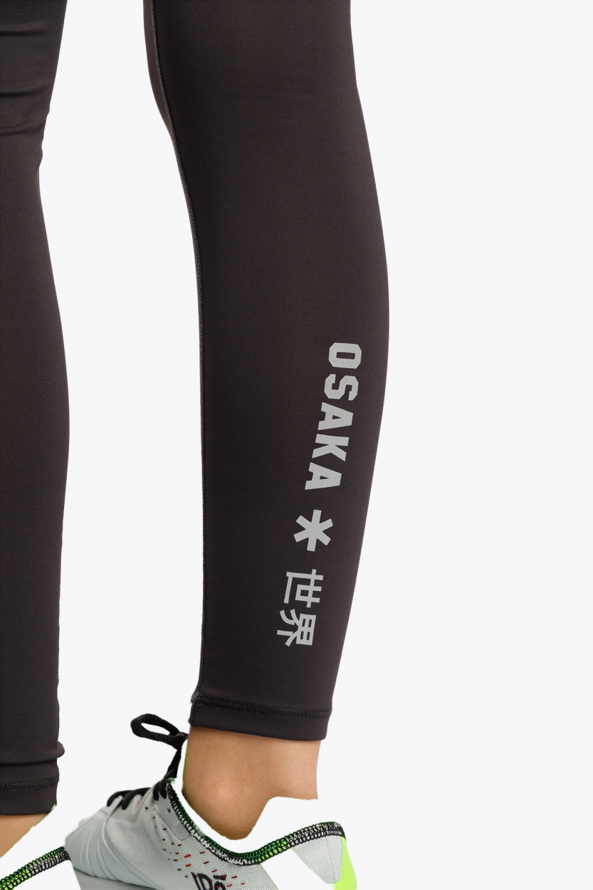 Model wearing the Osaka Kids Baselayer Tights in Black. Detail logo view