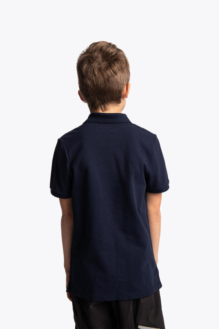 Boy wearing the Osaka kids polo in navy with logo in white. Back view