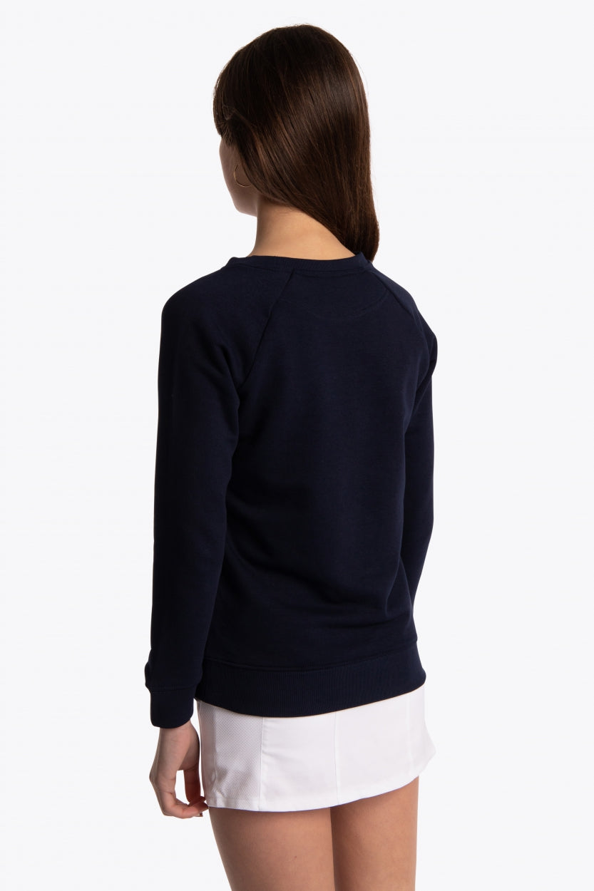 Girl wearing the Osaka kids sweater in navy with logo in blue. Side/back view