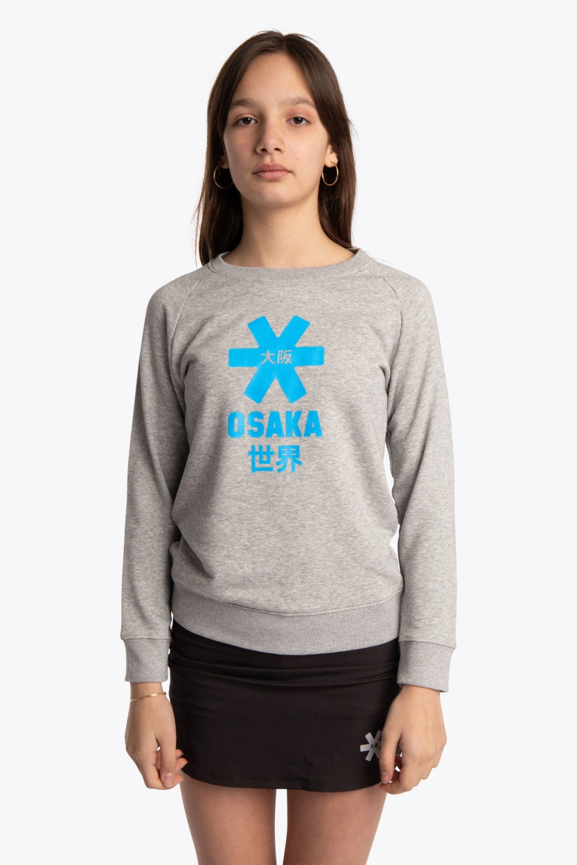 Girl wearing the Osaka kids sweater in grey with logo in blue. Front view
