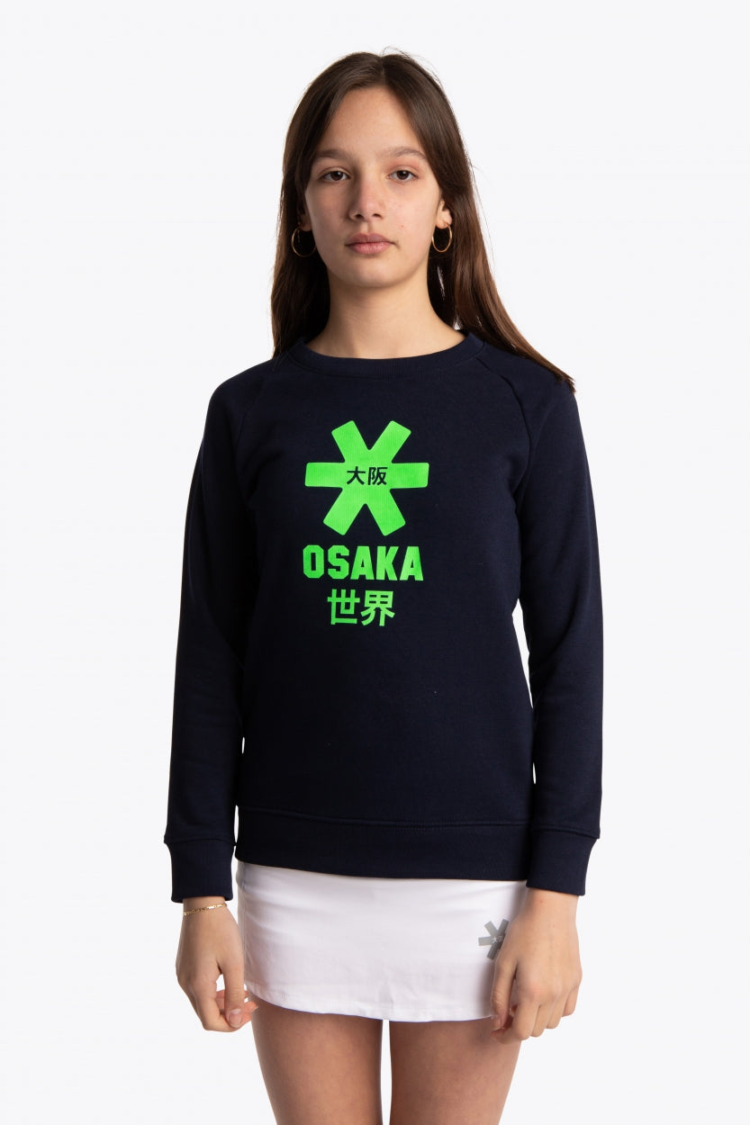 Girl wearing the Osaka kids sweater in navy with logo in green. Front view