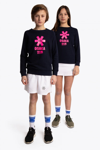 Boy and girl wearing the Osaka kids sweater in navy with pink logo. Full front view