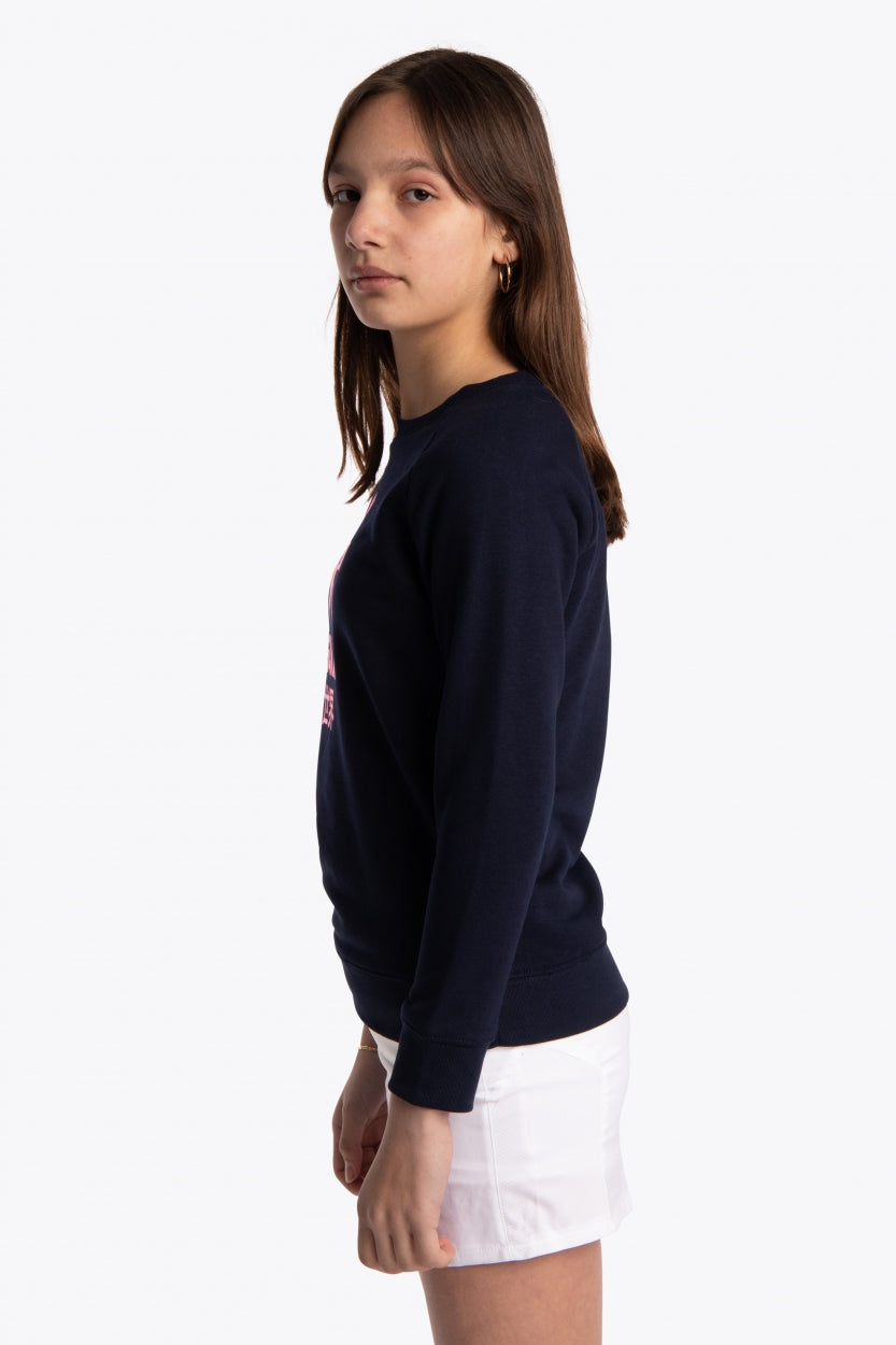 Girl wearing the Osaka kids sweater in navy with pink logo. Side view
