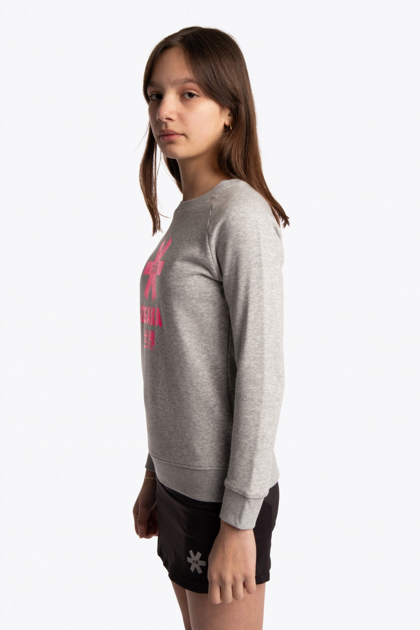 Girl wearing the Osaka kids sweater in grey with pink logo. Side view