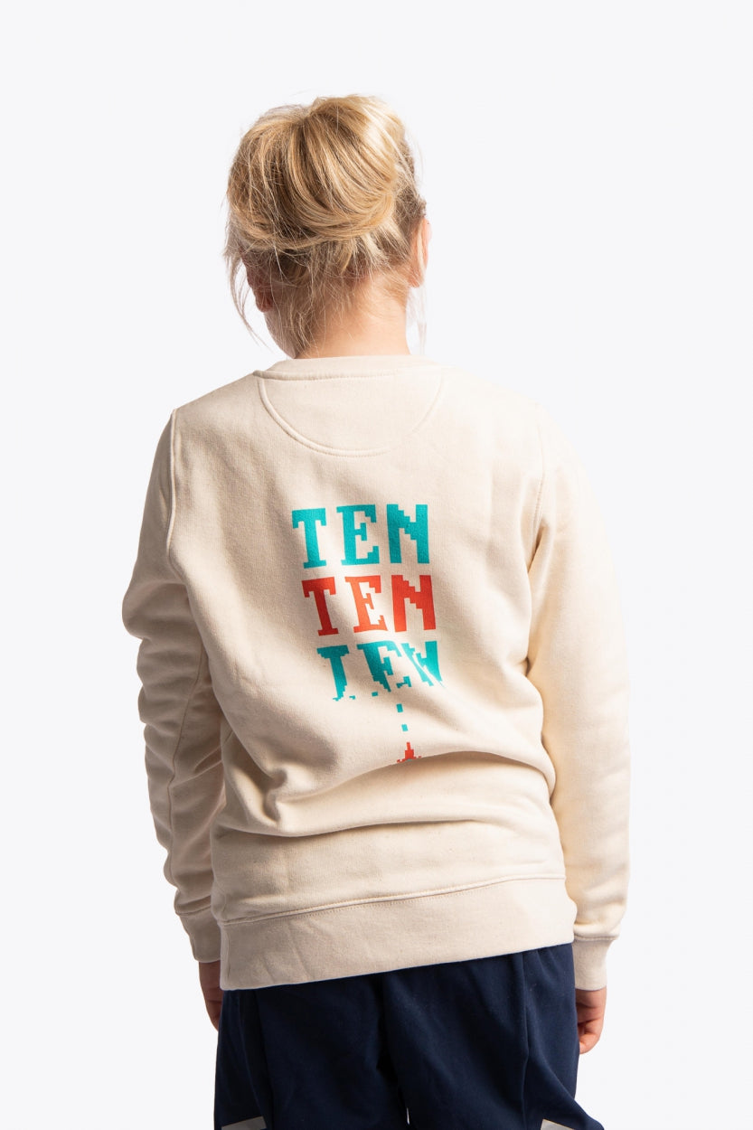 Girl wearing the Osaka kids pixo sweater in natural raw with orange and blue logo. Back view