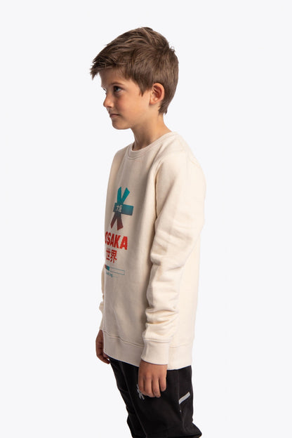 Boy wearing the Osaka kids pixo sweater in natural raw with orange and blue logo. Side view