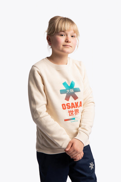 Girl wearing the Osaka kids pixo sweater in natural raw with orange and blue logo. Front view