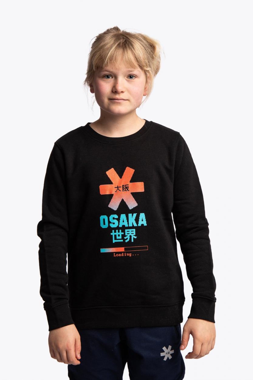 Girl wearing the Osaka kids pixo sweater in black with orange and blue logo. Front view