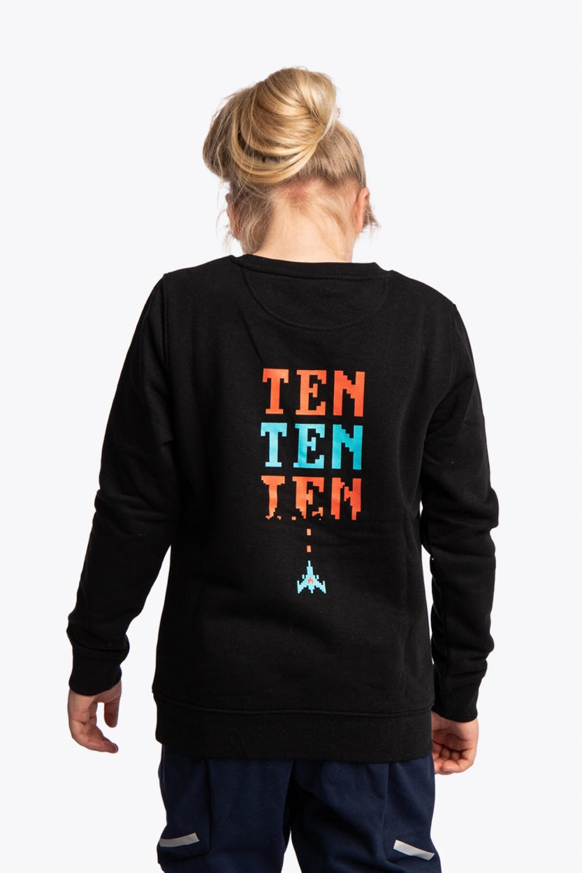 Girl wearing the Osaka kids pixo sweater in black with orange and blue logo. Back view