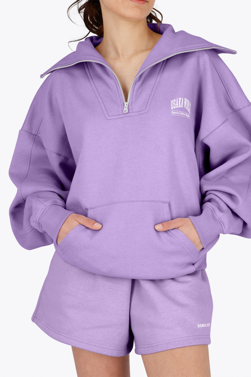 Woman wearing the Osaka women half zip sweater in light purple with white logo. Front  view