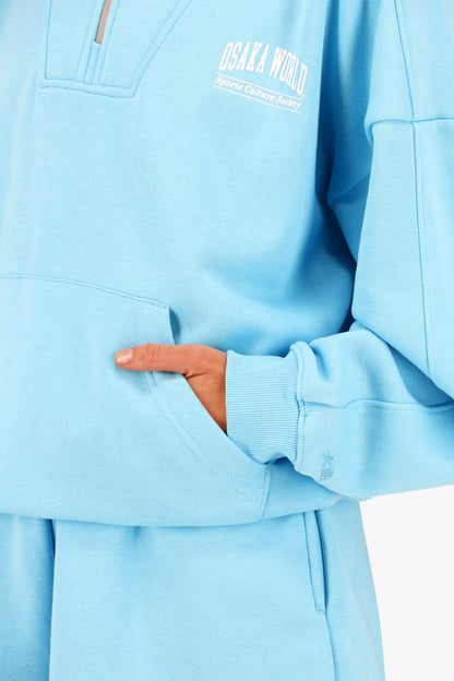 Osaka women half zip sweater in light blue with white logo. Front detail sleeve view