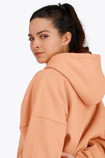 Woman wearing the Osaka women hoodie in peach with white logo. Back detail cap view
