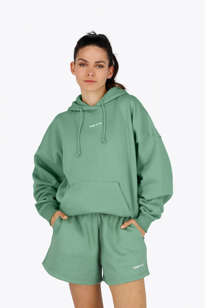 Woman wearing the Osaka women hoodie in green with white logo. Front view