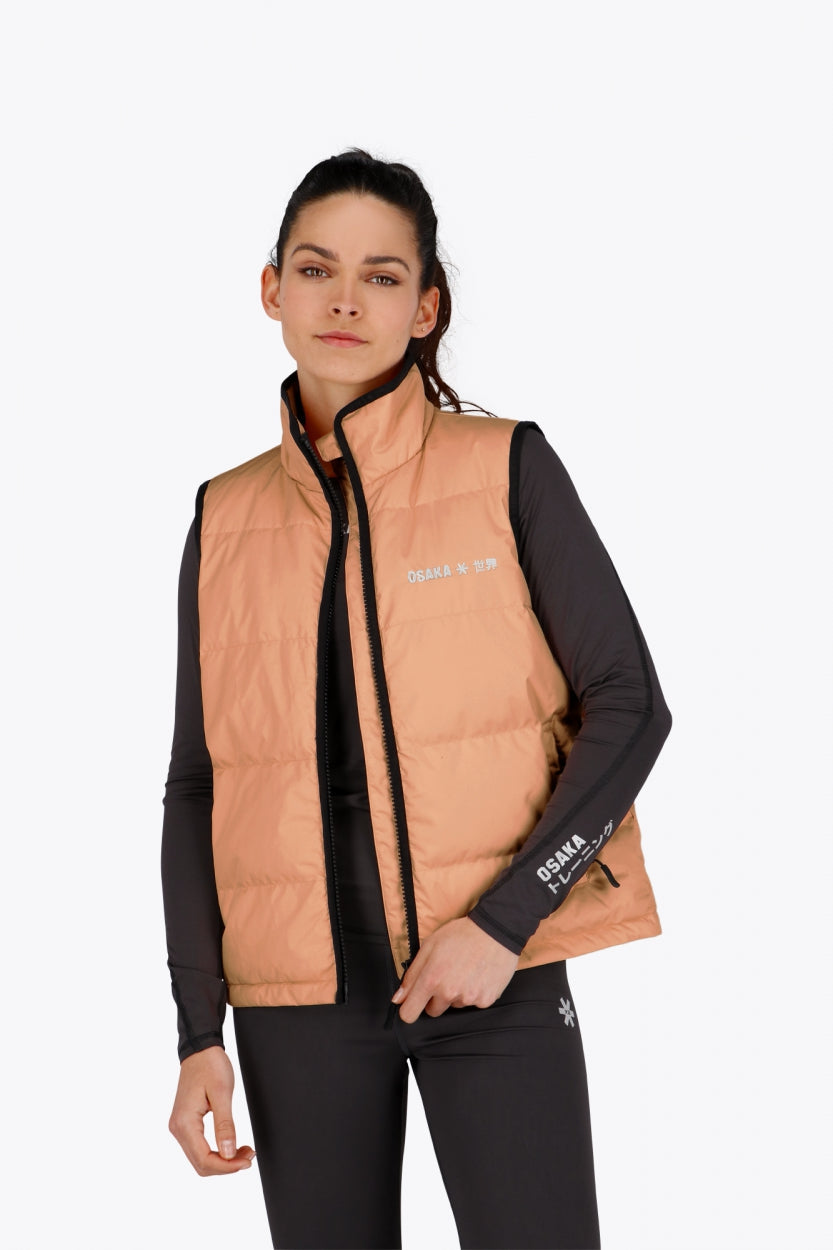Woman wearing the Osaka women padded gilet in peach with grey logo. Front view