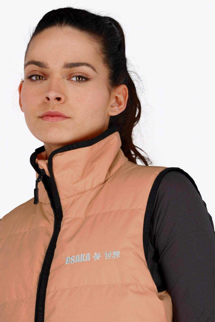 Woman wearing the Osaka women padded gilet in peach with grey logo. Front detail logo view