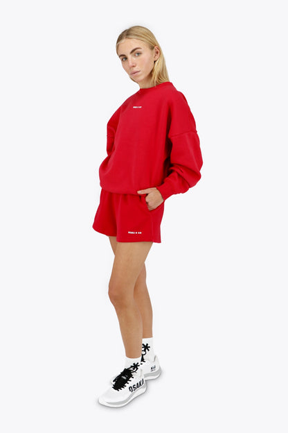 Woman wearing the Osaka women sweater in red with logo in white. Front / side view
