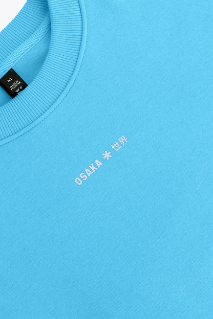 Osaka women sweater in light blue with logo in white. Front flatlay detail logo view