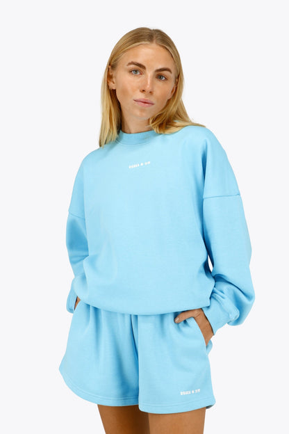 Woman wearing the Osaka women sweater in light blue with logo in white. Front view