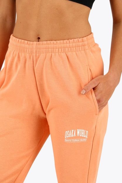 Woman wearing the Osaka women sweatpants in peach with logo in white. Front detail logo view