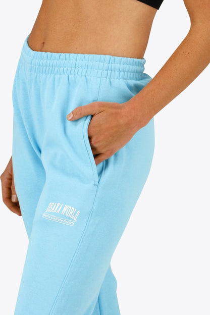 Woman wearing the Osaka women sweatpants in light blue with logo in white. Front detail logo view
