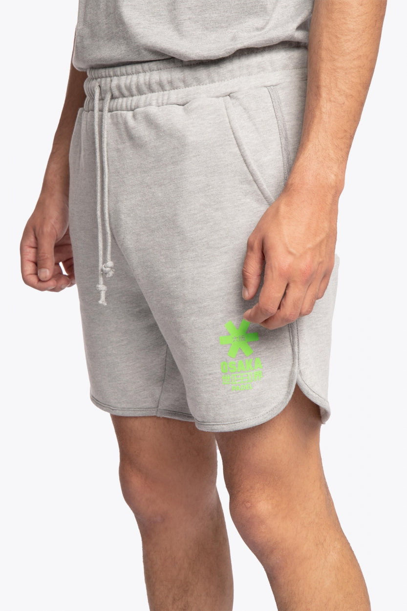 Man wearing the Osaka Men padel shorts in grey with green logo on it. Front / side view