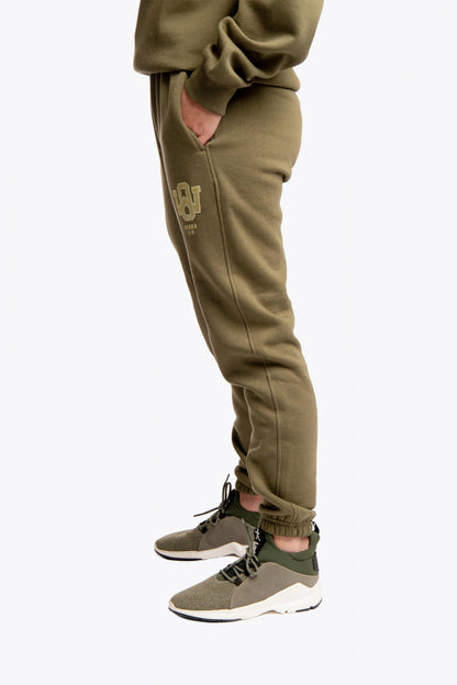 Model wearing the Osaka unisex sweatpants in army green with logo in yellow.  Side view