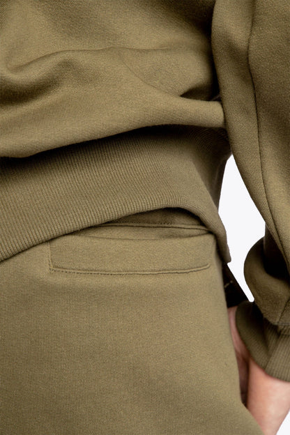 Model wearing the Osaka unisex sweatpants in army green with logo in yellow.  Detail back pocket view