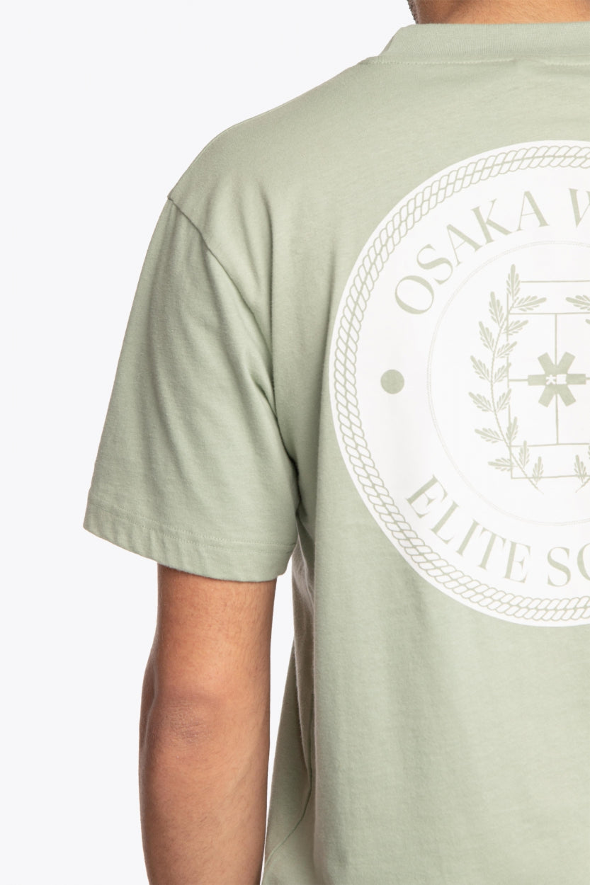 Man wearing the Osaka unisex tee in iceberg green with white logo. Detail back logo view