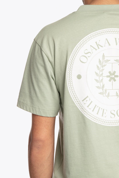 Man wearing the Osaka unisex tee in iceberg green with white logo. Detail back logo view