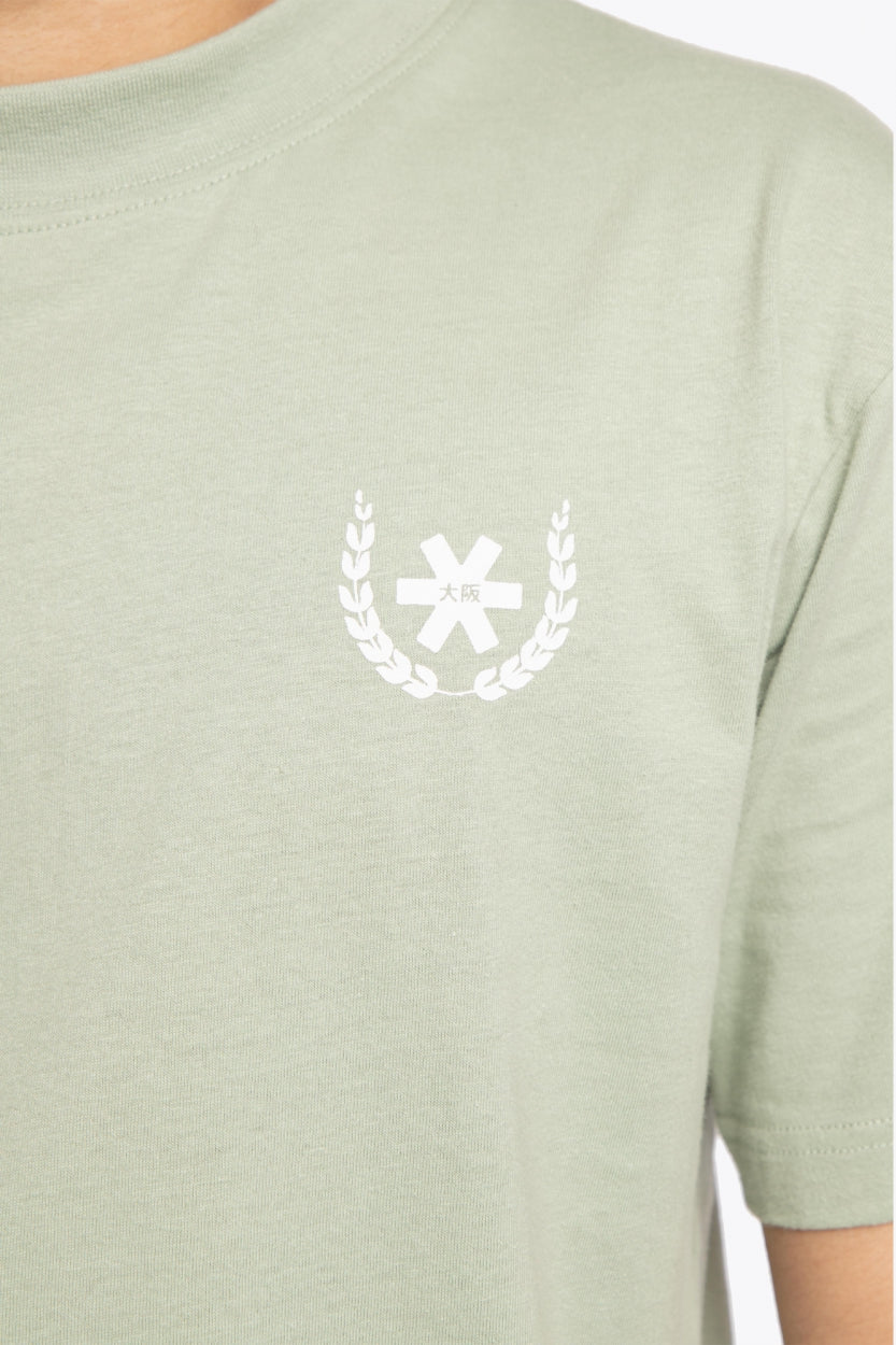 Man wearing the Osaka unisex tee in iceberg green with white logo. Detail front logo view