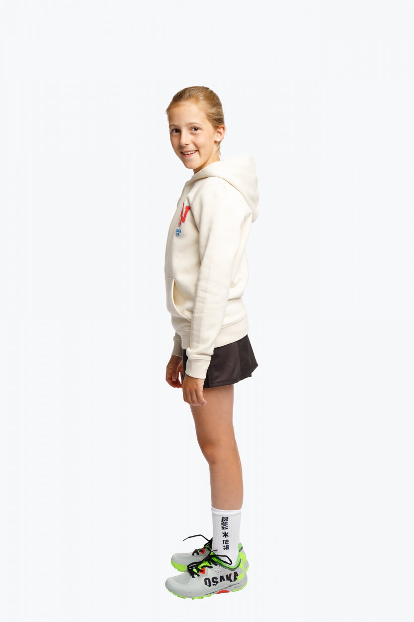 Girl wearing the Osaka kids hoodie in natural raw with college letters in orange and logo in blue. Side view