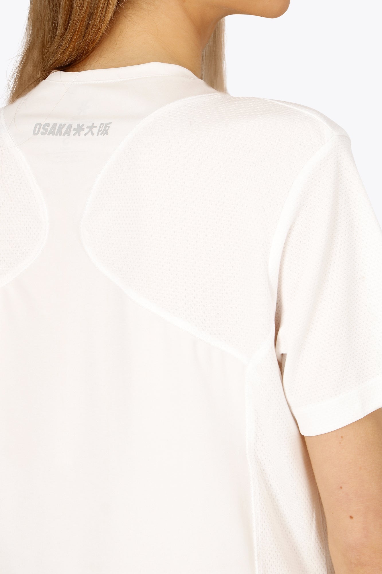 Woman wearing the Osaka women v-neck tech dress in white with logo in grey. Back detail logo view