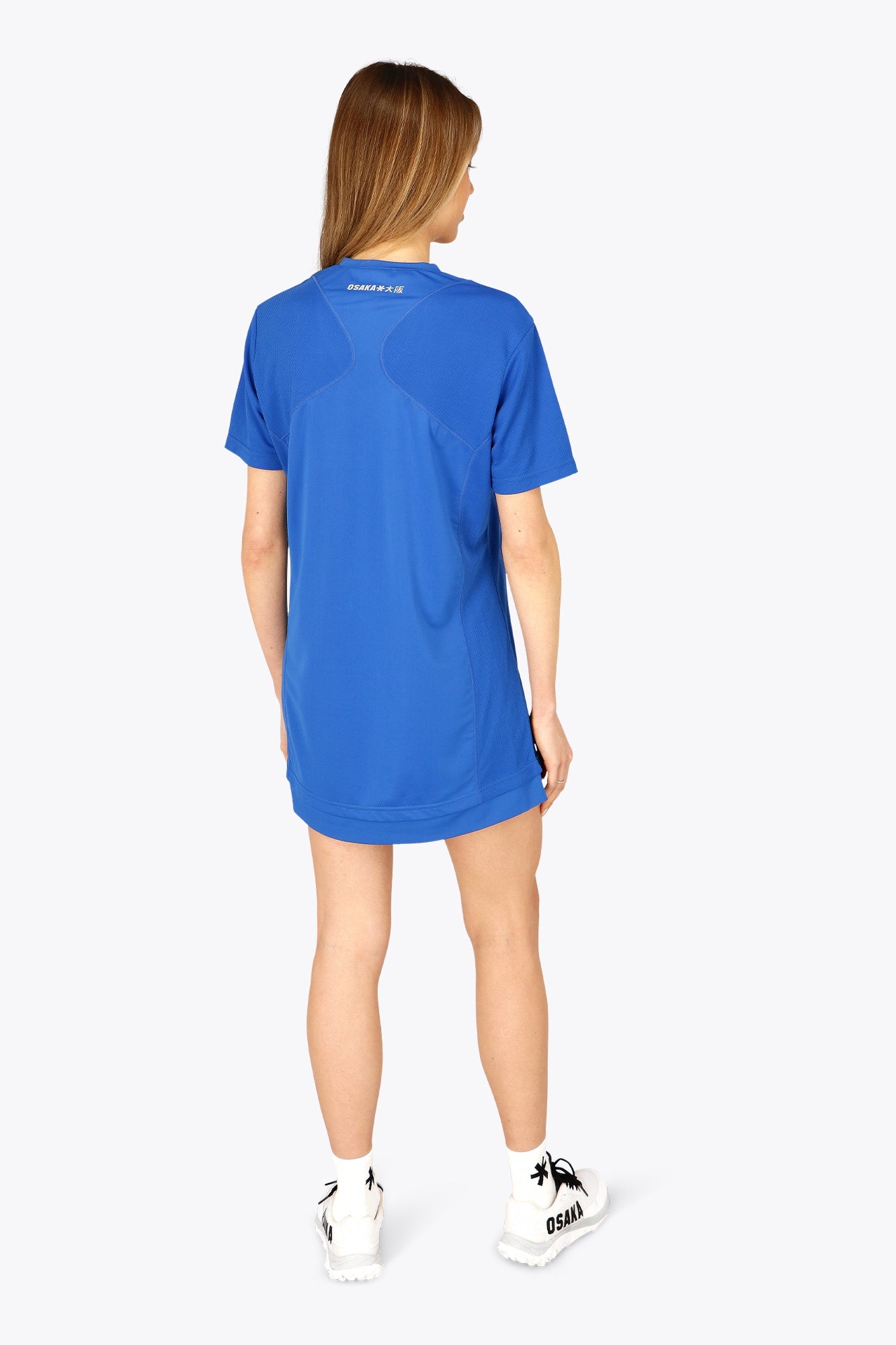 Woman wearing the Osaka women v-neck tech dress in princess blue with logo in grey. Back view