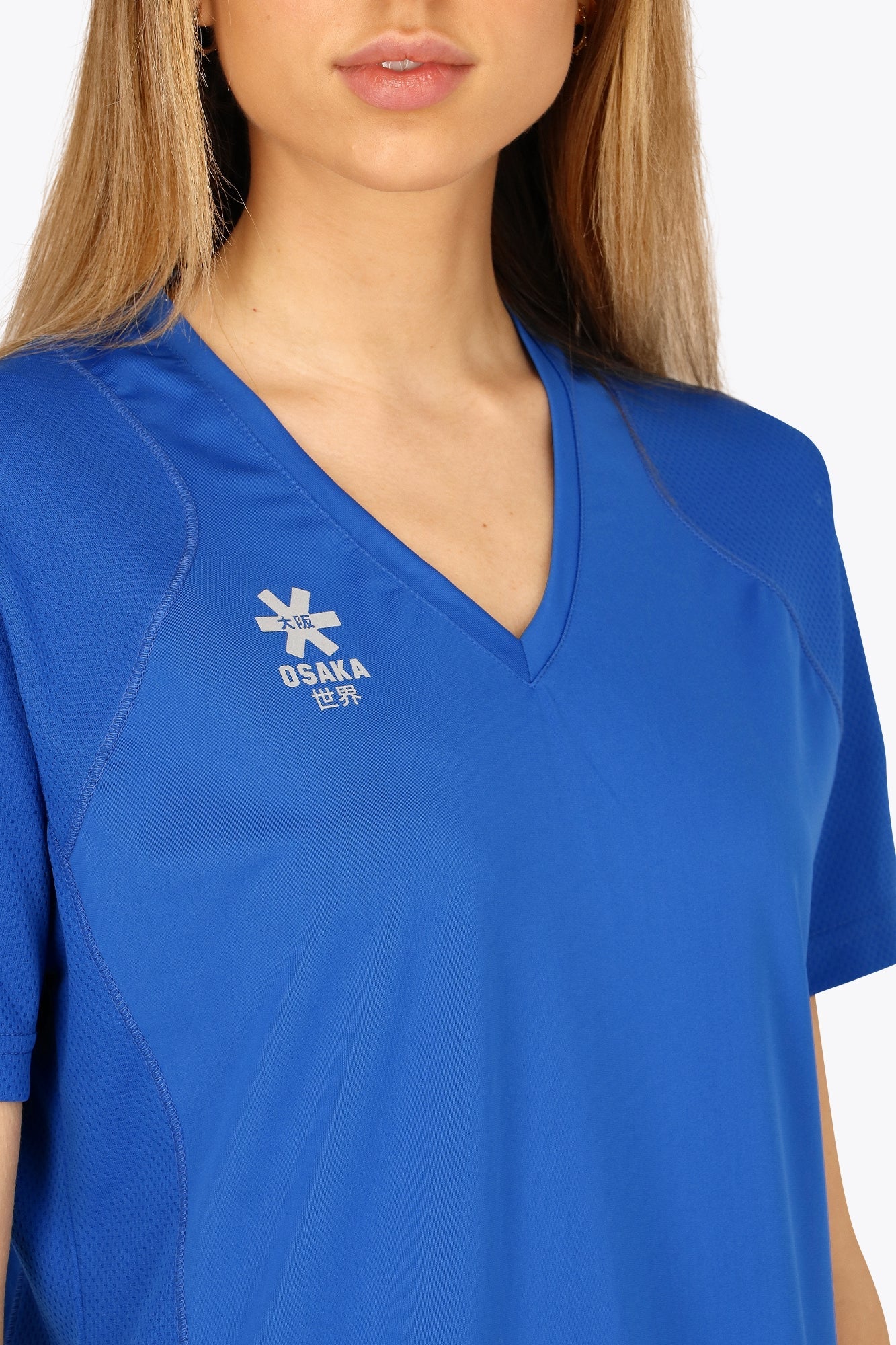 Woman wearing the Osaka women v-neck tech dress in princess blue with logo in grey. Front detail logo view