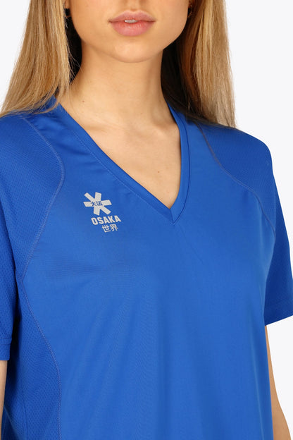 Woman wearing the Osaka women v-neck tech dress in princess blue with logo in grey. Front detail logo view