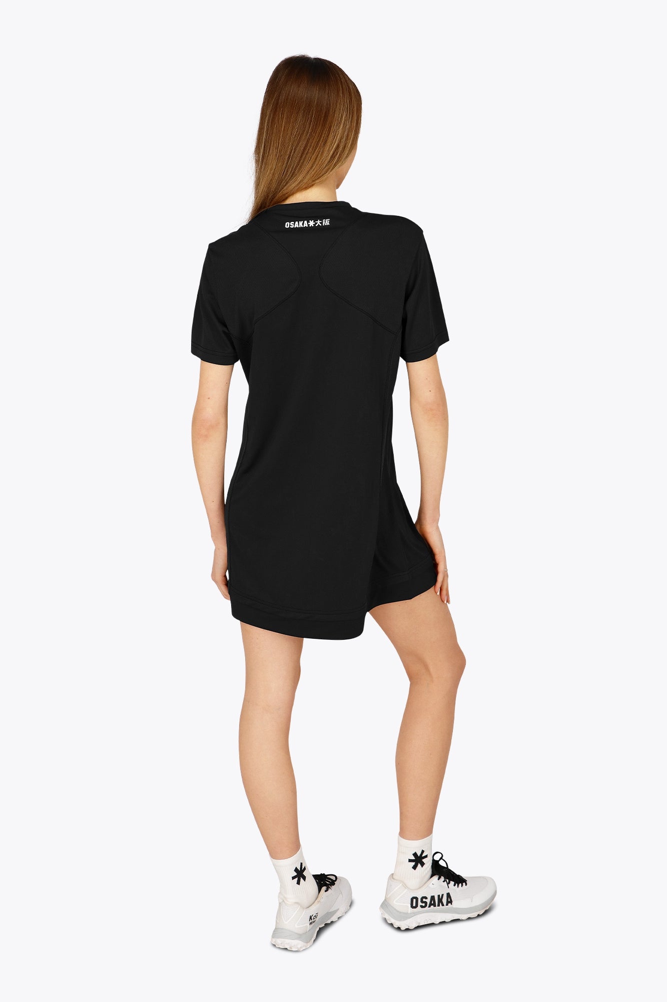 Woman wearing the Osaka women v-neck tech dress in black with logo in grey. Back view