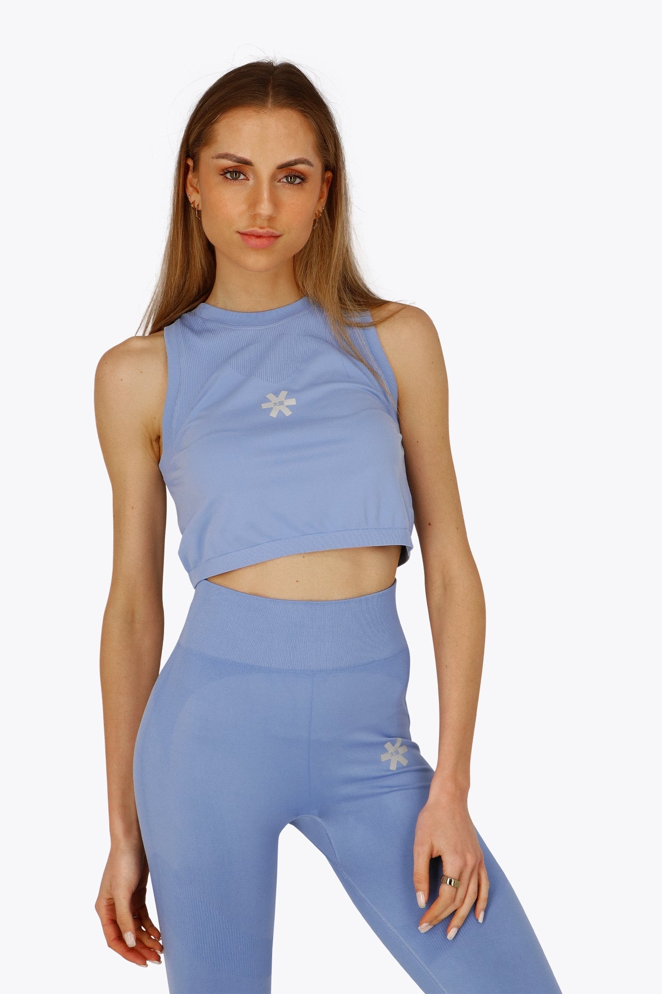 Woman wearing the Osaka women tech tank top in manor blue with logo in grey. Front view