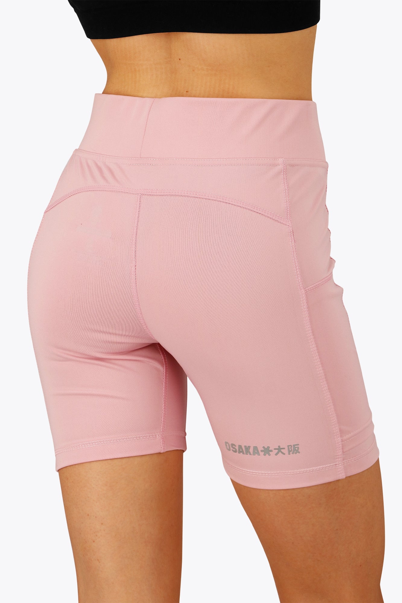 Woman wearing the Osaka women tech short thights in pink with grey logo. Back view