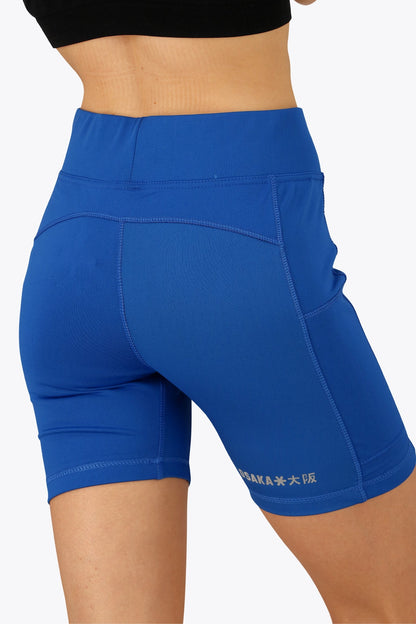 Woman wearing the Osaka women tech short thights in princess blue with grey logo. Back view