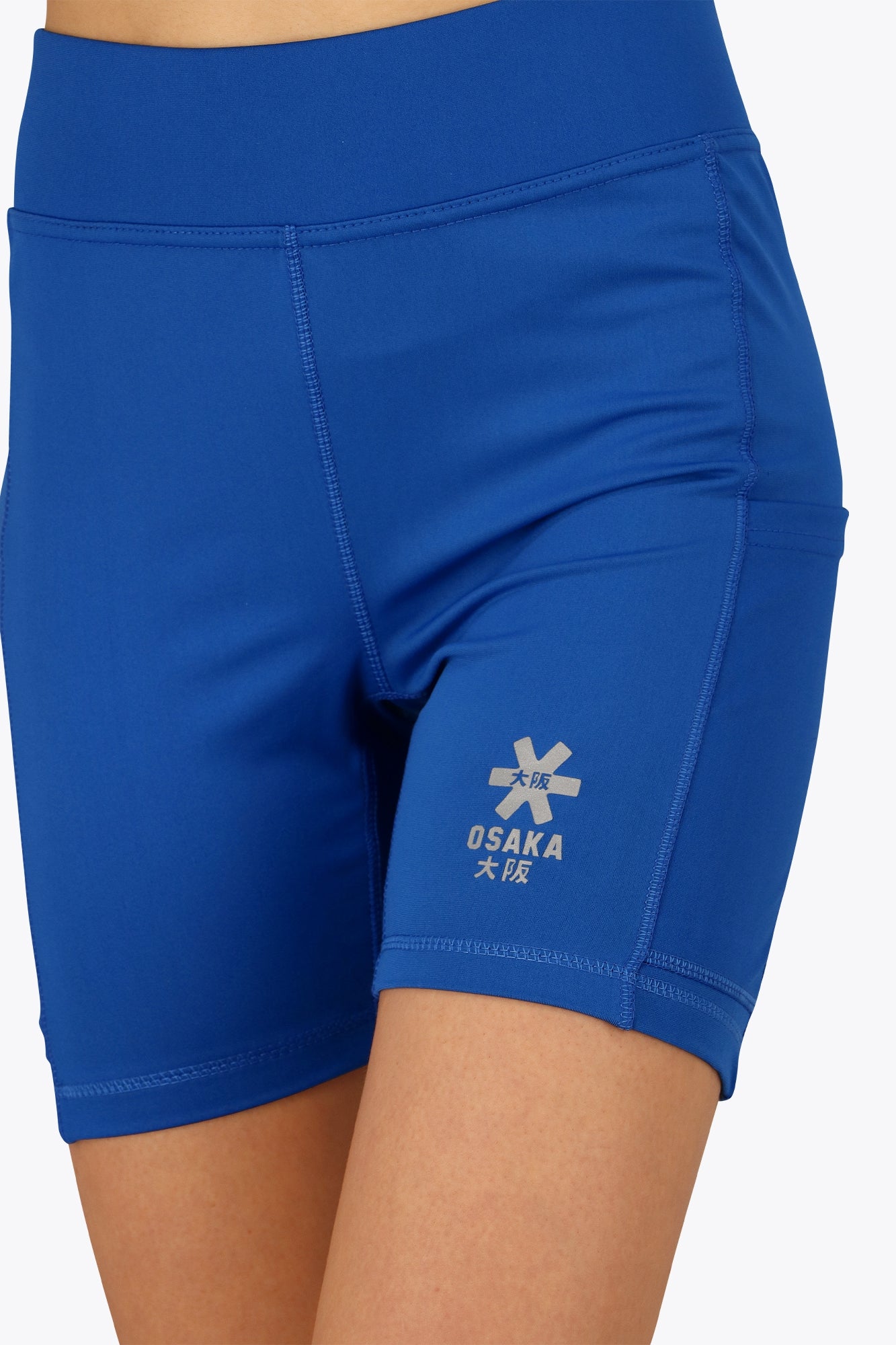 Woman wearing the Osaka women tech short thights in princess blue with grey logo. Front detail logo view