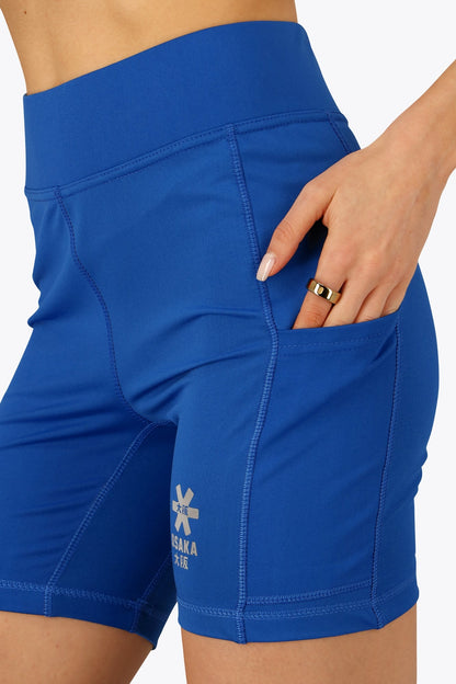 Woman wearing the Osaka women tech short thights in princess blue with grey logo. Front detail pocket view