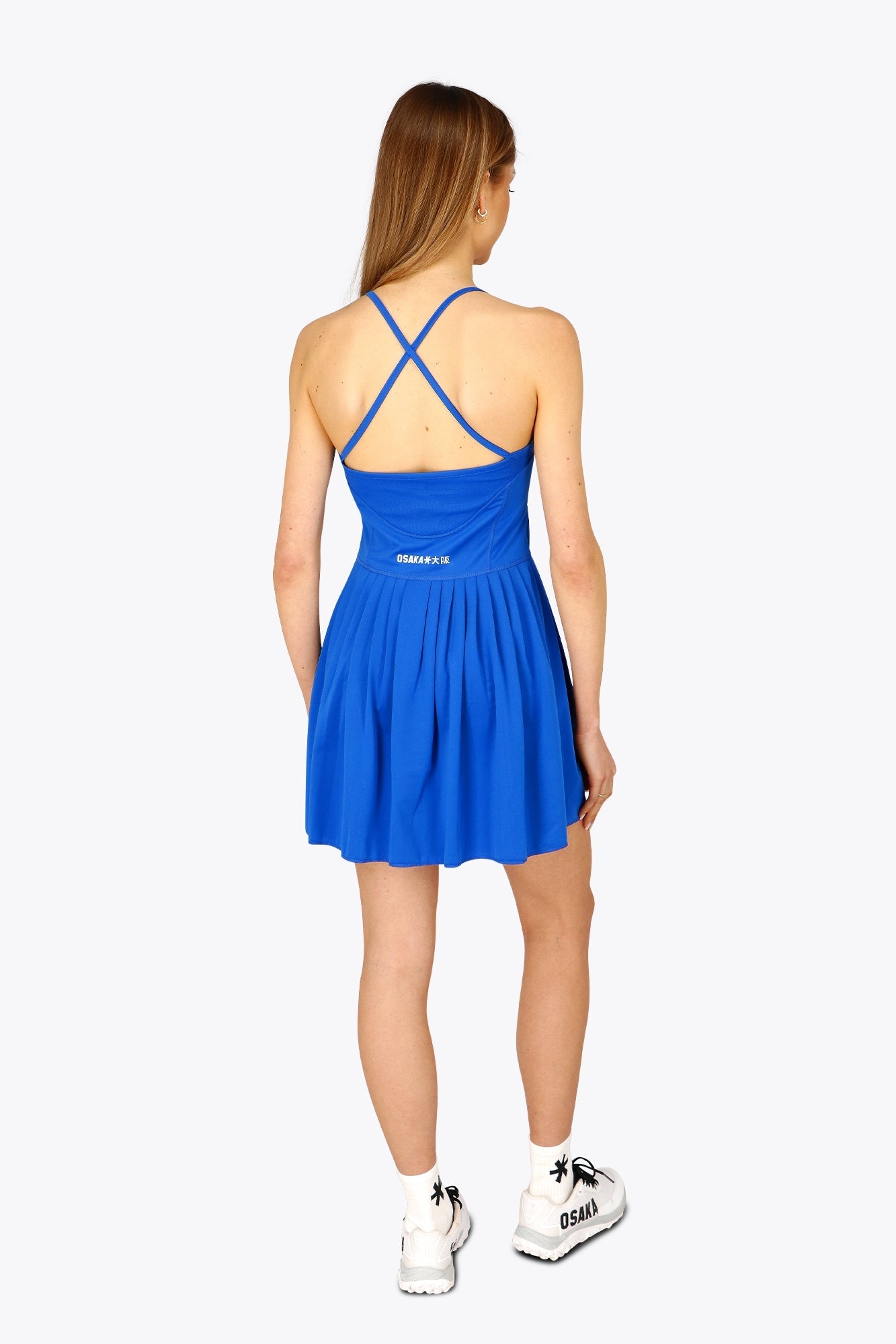 Woman wearing the Osaka women pleated tech dress in princess blue with grey logo. Back view