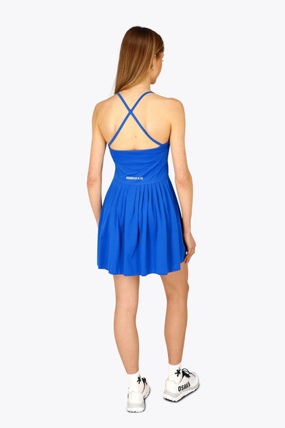 Woman wearing the Osaka women pleated tech dress in princess blue with grey logo. Back view