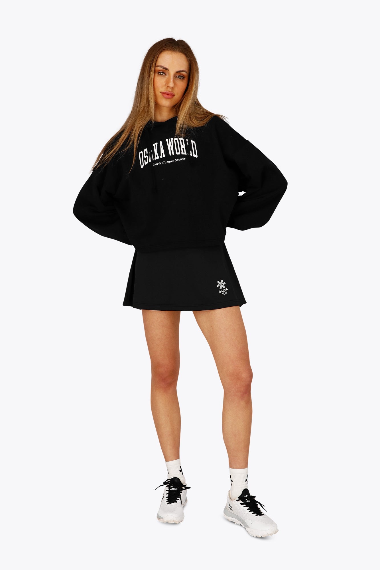 Woman wearing the Osaka women floucy skort black with logo in grey. Front view