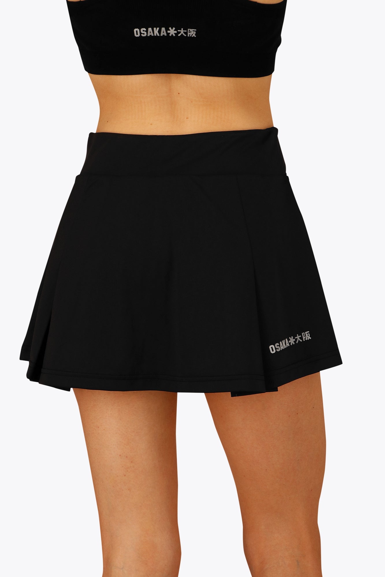 Woman wearing the Osaka women floucy skort black with logo in grey. Back detail view