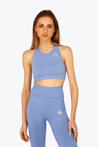 Woman wearing the Osaka women tech sports bra in manor blue with logo in grey. Front view
